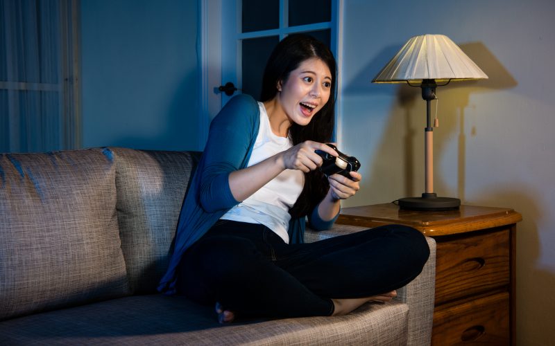 A woman sitting on a couch plays a video game.