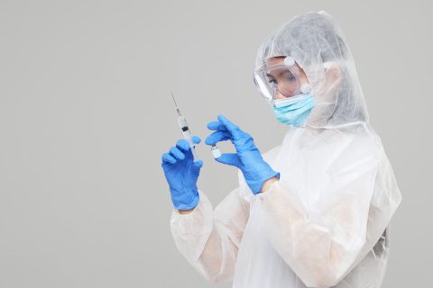 A healthcare worker wearing PPE prepares to give an injection.