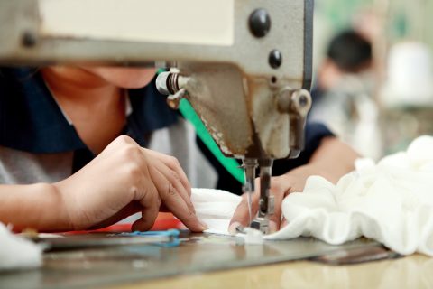 A portrait of worker using industrial sewing machine at garment factory.
