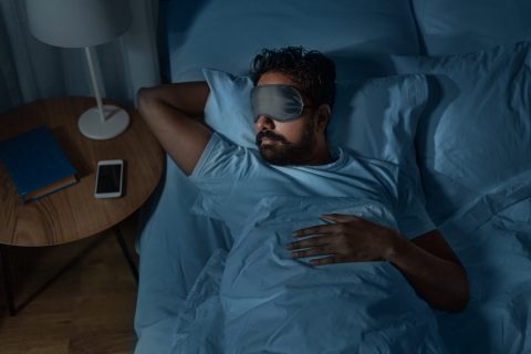 A man lays in bed with a sleeping mask on.