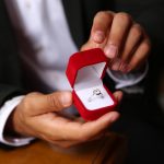 Person in a suit holds a wedding ring in a red box.