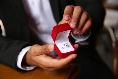 Person in a suit holds a wedding ring in a red box.
