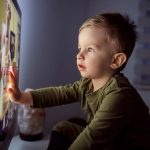 A toddler touches a lit-up TV screen