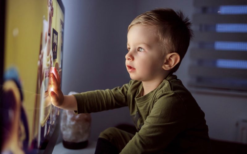 A toddler touches a lit-up TV screen