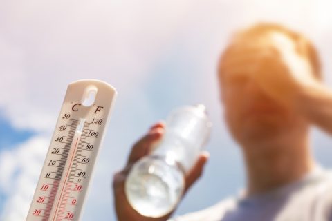 A man holding a water bottle stands in the heat in front of a thermometer