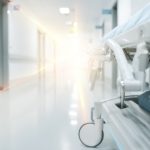 A hospital gurney is wheeled down a hall with a light at the end of the hallway