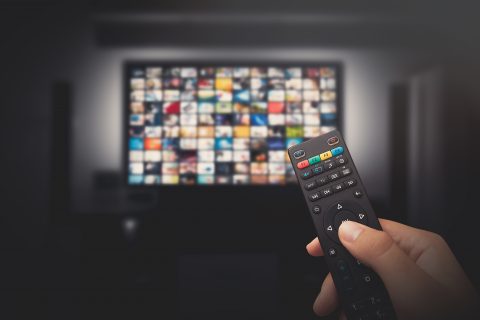 Someone points a remote control at a TV with lots of shows