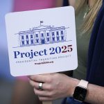 A hand holds a sign that says Project 2025