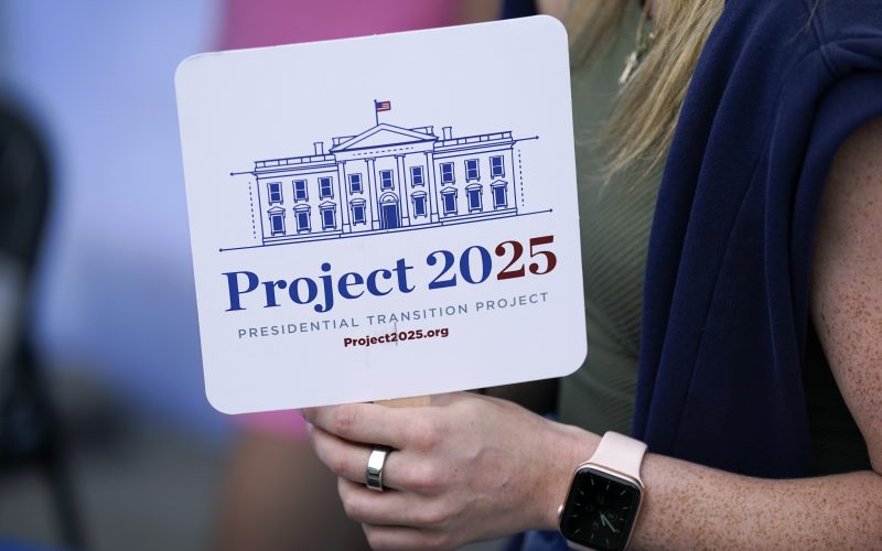 A hand holds a sign that says Project 2025