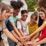 A small group of young people touch hands in the middle of a circle ahead of a cheer.