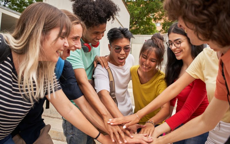 A small group of young people touch hands in the middle of a circle ahead of a cheer.