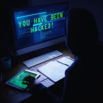 A shadowy figure sits in front of a computer screen that reads "YOU HAVE BEEN HACKED!"