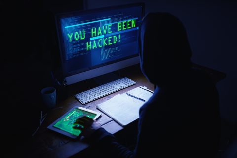 A shadowy figure sits in front of a computer screen that reads "YOU HAVE BEEN HACKED!"