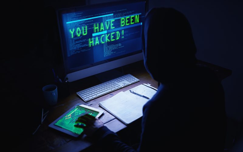 A shadowy figure sits in front of a computer screen that reads "YOU HAVE BEEN HACKED!"