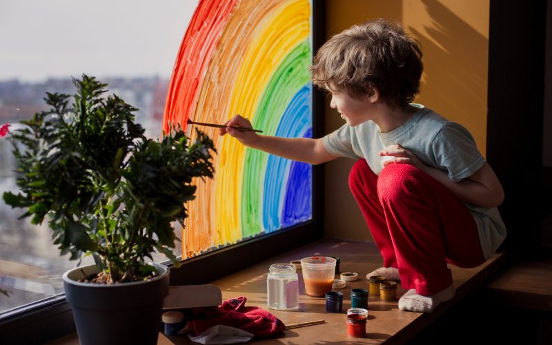 A child painting a rainbow on a window