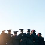 College graduates linking arms, shown from behind