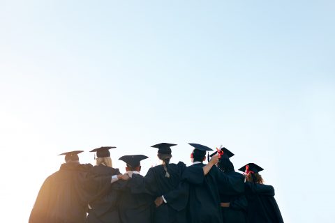 College graduates linking arms, shown from behind